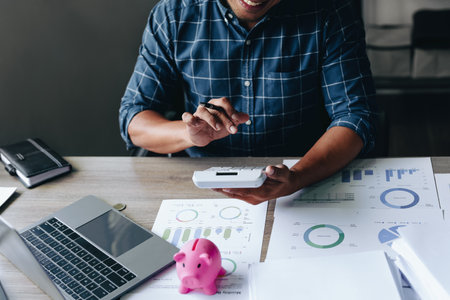 Portrait of an Asian businessman using a calculator to calculate his savings from SME operations, with a pink piggy bank as keep money concept.の写真素材