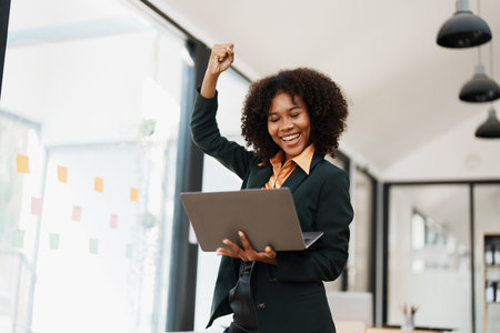 Beautiful young teen American African business women holding computer laptop with hands up in winner is gesture, Happy to be successful celebrating achievement success.の写真素材