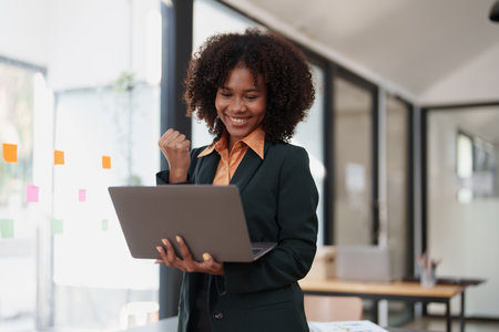 Beautiful young teen American African business women holding computer laptop with hands up in winner is gesture, Happy to be successful celebrating achievement success.の写真素材