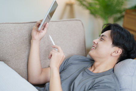 Portrait of an Asian teenager using a digital tablet on the sofa while relaxing at home.の写真素材