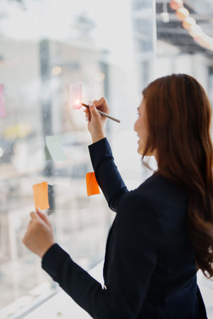 Beautiful young teen asian businesswoman using note pad thinking with planning working on financial...