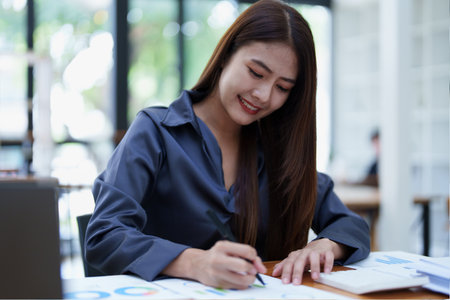 A portrait of an Asian female accountant with a smiling face sits and uses a calculator to calculate taxes for companies to submit evidence to the Revenue Department.の写真素材