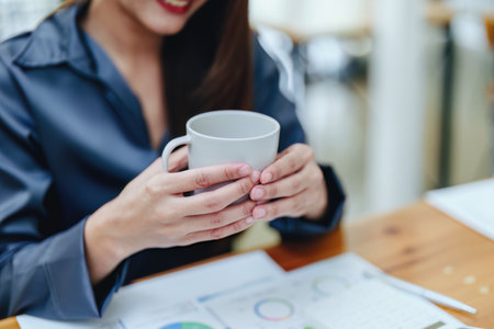 Portrait of a happy Asian woman smiling at her desk during the daytime coffee break.の写真素材