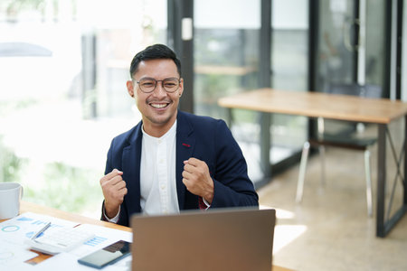 Portrait of an Asian male business owner standing with a computer showing happiness after a successful investment.の写真素材