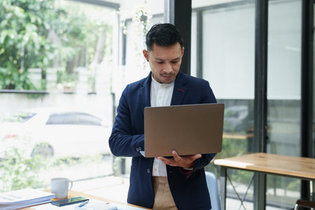 Portrait of an Asian male business owner standing using a computer to analyze work.