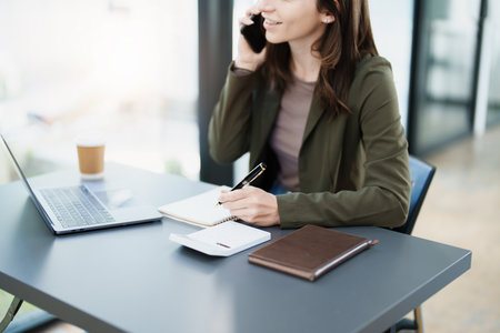 Portrait of a young Asian Woman showing a smiling face as she uses his smartphone mobile, notebook and computer laptop on her desk in the early morning hoursの写真素材