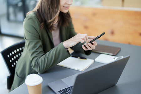 Portrait of a young Asian man showing a smiling face as she uses his phone, computer and financial documents on her desk in the early morning hours.の写真素材