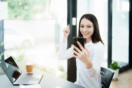 Excited businesswoman using mobile phone while in officeの写真素材