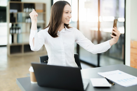 Excited businesswoman using mobile phone while in office , business conceptsの写真素材