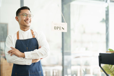Portrait of a beautiful Asian man running a small business showing a smiling face, a coffee shop owner opening a shop to welcome customers in the new morning, SME concepts.の写真素材