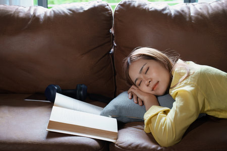 Portrait of Asian woman resting while reading a book on sofa at home.の写真素材