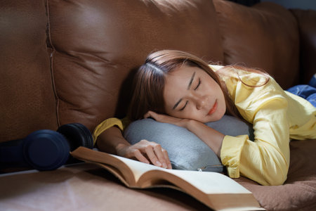 Portrait of Asian woman resting while reading a book on sofa at home.の写真素材