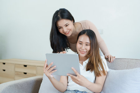 lgbtq, lgbt concept, homosexuality, portrait of two asian women posing happy together and loving each other while playing tablet at sofa.の写真素材