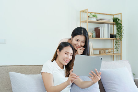 lgbtq, lgbt concept, homosexuality, portrait of two asian women posing happy together and loving each other while playing tablet at sofa.の写真素材