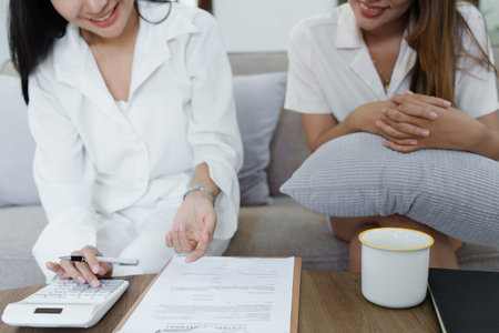 Portrait of young Asian female agent offering life insurance to client using document, calculator and tablet in product presentation.の写真素材
