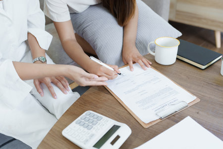 Portrait of young Asian female agent offering life insurance to client using document, calculator...