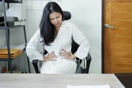 Portrait of a young Asian female representative showing acute abdominal pain from sitting for a long time at work. High quality photoの写真素材