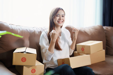 Starting small business entrepreneur of independent Asian woman smiling using computer laptop with cheerful success of online marketing package box items and SME delivery concept.の写真素材