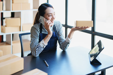 Starting small business entrepreneur of independent Asian female online seller talking on the phone with a customer and packing products for delivery to the customer. and SME delivery concept.の写真素材