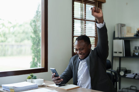 middle aged man American African business man holding smart phone mobile with hands up in winner is gesture, Happy to be successful celebrating achievement success.の写真素材