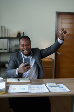 middle aged man American African business man holding smart phone mobile with hands up in winner is gesture, Happy to be successful celebrating achievement success.の写真素材