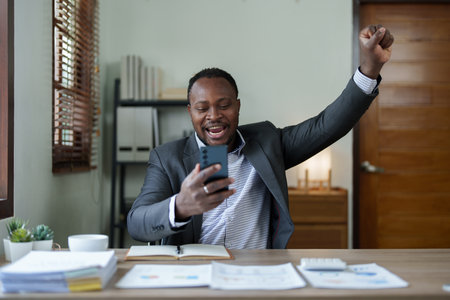 middle aged man American African business man holding smart phone mobile with hands up in winner is gesture, Happy to be successful celebrating achievement success.の写真素材