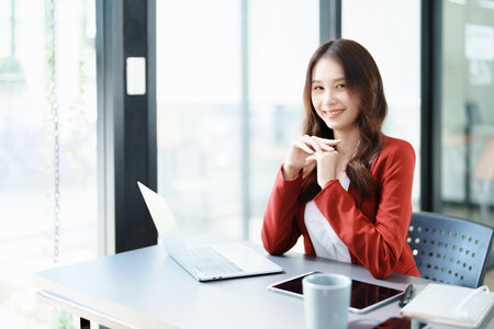 Portrait of a woman business owner showing a happy smiling face as he has successfully invested her business using computers and financial budget documents at work.の写真素材