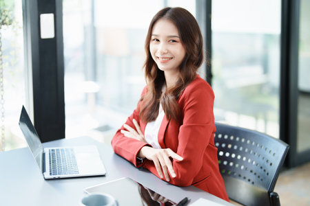 Portrait of a woman business owner showing a happy smiling face as he has successfully invested her business using computers and financial budget documents at work.の写真素材