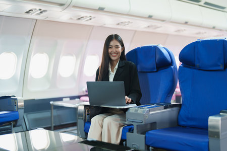 Asian business woman passenger sitting on business class plane while working on laptop computer with simulated space using on board wireless connection.の写真素材