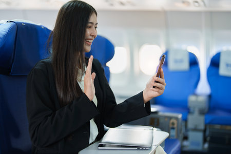 Asian business woman passenger sitting on business class luxury plane while working using smart phone mobile talking or video conference and travel concept.の写真素材