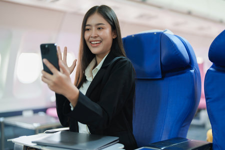 Asian business woman passenger sitting on business class luxury plane while working using smart phone mobile talking or video conference and travel concept.の写真素材