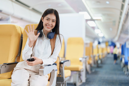 Young asian attractive woman travel by airplane, Passenger wearing headphone putting hand baggage in lockers above seats of plane.の写真素材