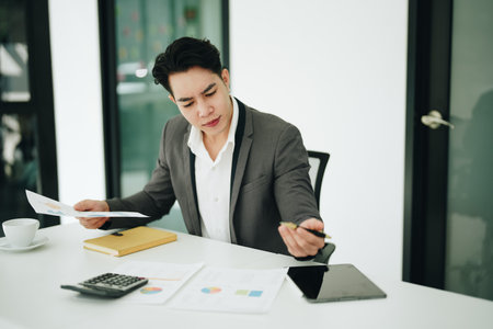 businessman or accountant working on calculator and laptop computer to calculate business data during using accountancy document at officeの写真素材