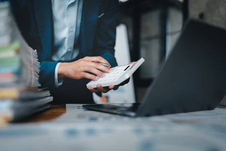 Young asian male work with financial papers at home count on calculator before paying taxes receipts online, planning budget glad to find chance for economy saving money, audit conceptsの写真素材