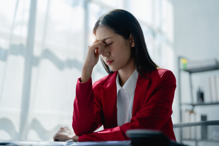 Portrait of a young Asian woman showing acute headache from sitting for a long time at workの写真素材
