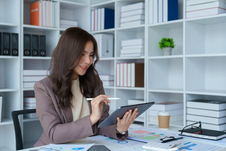 businesswoman in a black suit inside the office using tablet computer, audit paperwork for customers to contact, business people conceptの写真素材