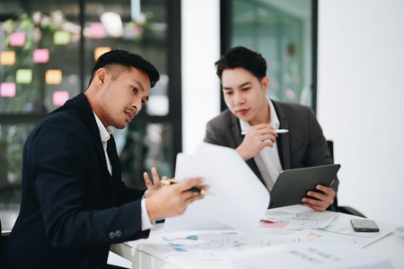 Two business men meeting to talking or discuss marketing work in workplace using paperwork, calculator, computer to workの写真素材