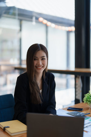 Portrait of a woman business owner showing a happy smiling face as he has successfully invested her business using computers and financial budget documents at work.の写真素材