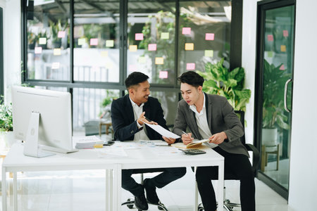 Two business men meeting to talking or discuss marketing work in workplace using paperwork, calculator, computer to workの写真素材