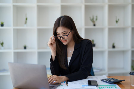 Young asian businesswoman manager, lawyer or company employee holding accounting bookkeeping documents checking financial data or marketing report working in office with laptop. Paperwork management.の写真素材