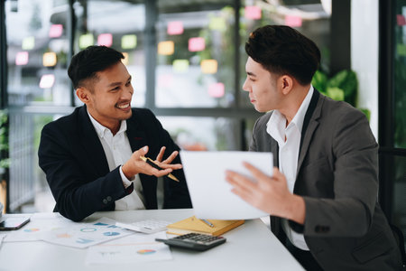 Two business men meeting to talking or discuss marketing work in workplace using paperwork, calculator, computer to workの写真素材