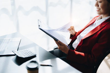 Young asian female work with financial papers at home count on calculator before paying taxes receipts online, planning budget glad to find chance for economy saving money, audit concepts.の写真素材