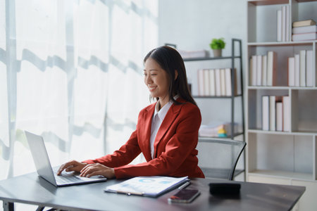 Beautiful young teen asian businesswoman using laptop computer and paperworks with planning working on financial document, tax, exchange, accounting and Financial advisor.の写真素材