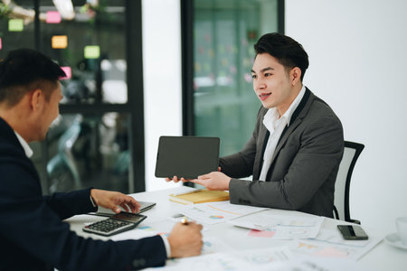 Two business men meeting to talking or discuss marketing work in workplace using paperwork, calculator, computer to workの写真素材