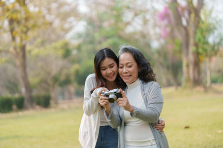 Asian teenage mother and daughter walking in park with camera to capture memories.