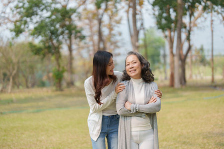Grown daughter with aging mother showing love and walking together in the parkland.