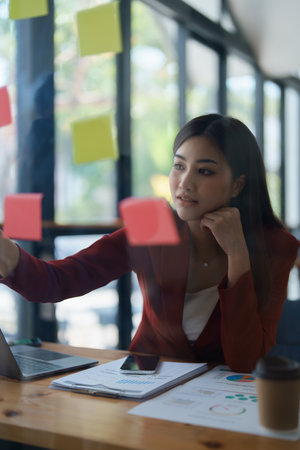 Beautiful young teen asian businesswoman using note pad thinking with planning working on financial...