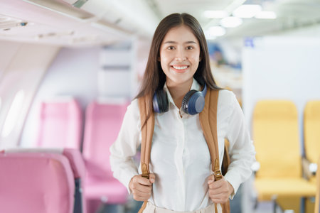 Young asian attractive woman travel by airplane, Passenger wearing headphone putting hand baggage in lockers above seats of plane.の写真素材