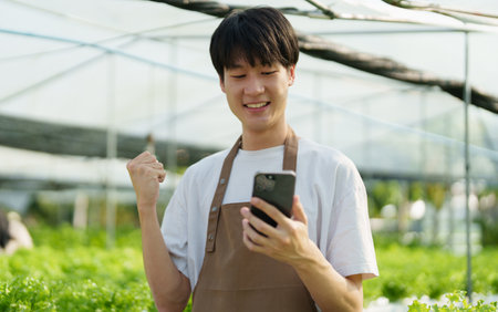 A farmer uses a phone to look at orders from customers, showing joy at harvesting vegetables from hydroponic farms. organic fresh vegetables Farmer working on a hydroponic vegetable gardenの写真素材