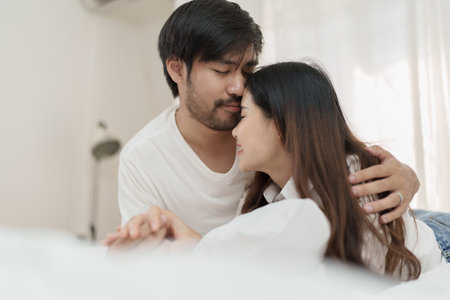 Asian Romantic couple in bed enjoying sensual foreplay Happy sensual young couple lying in bed together. Beautiful loving couple kissing in bedの写真素材
